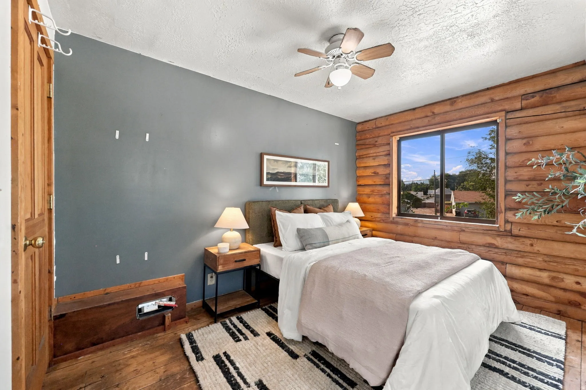 Wood-paneled accent wall with a window, wood-finish flooring, and a ceiling fan with integrated lighting
