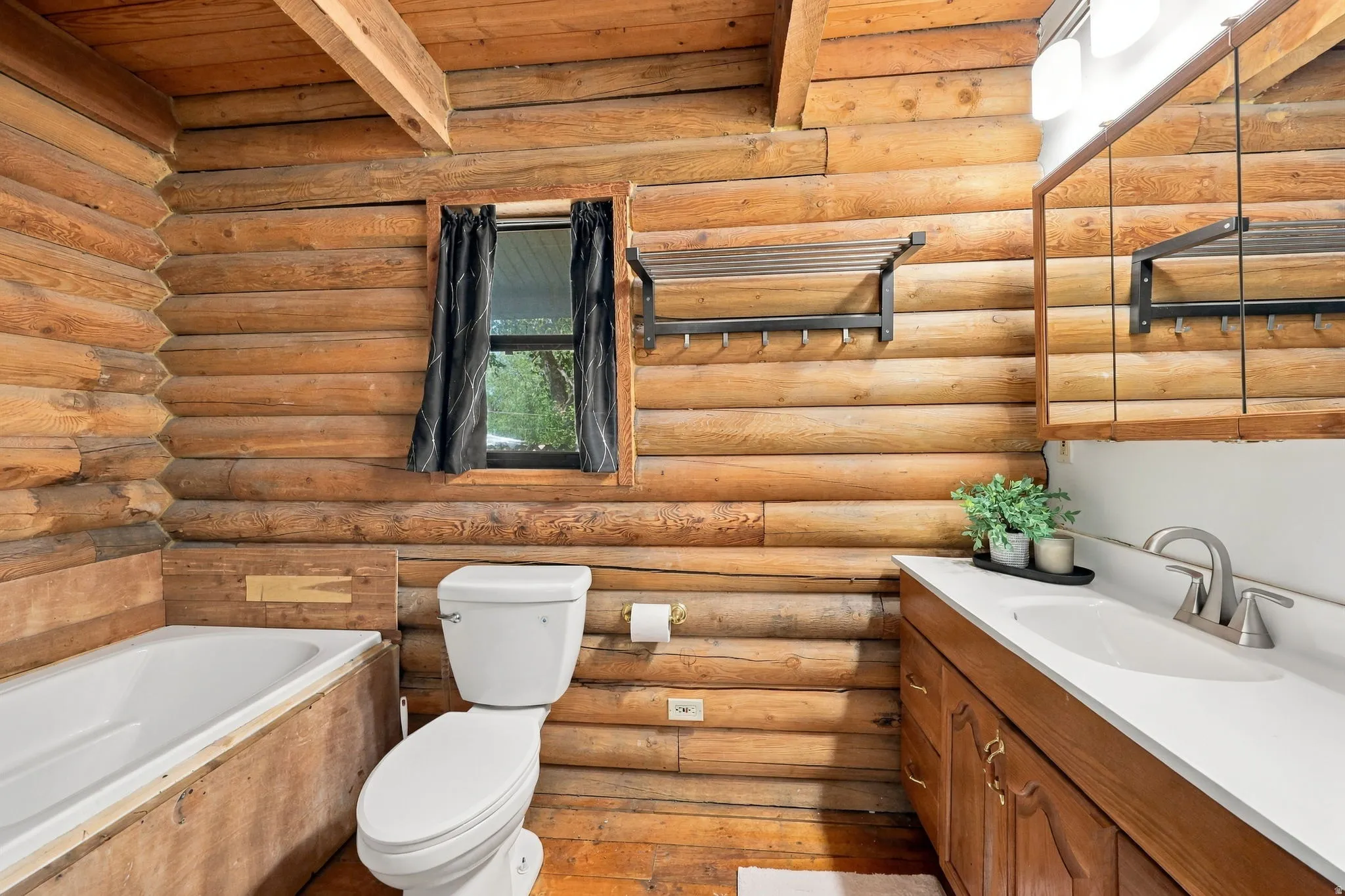 Log wall construction, wood-finish flooring, white vanity countertop, built-in medicine cabinet, and a white porcelain toilet