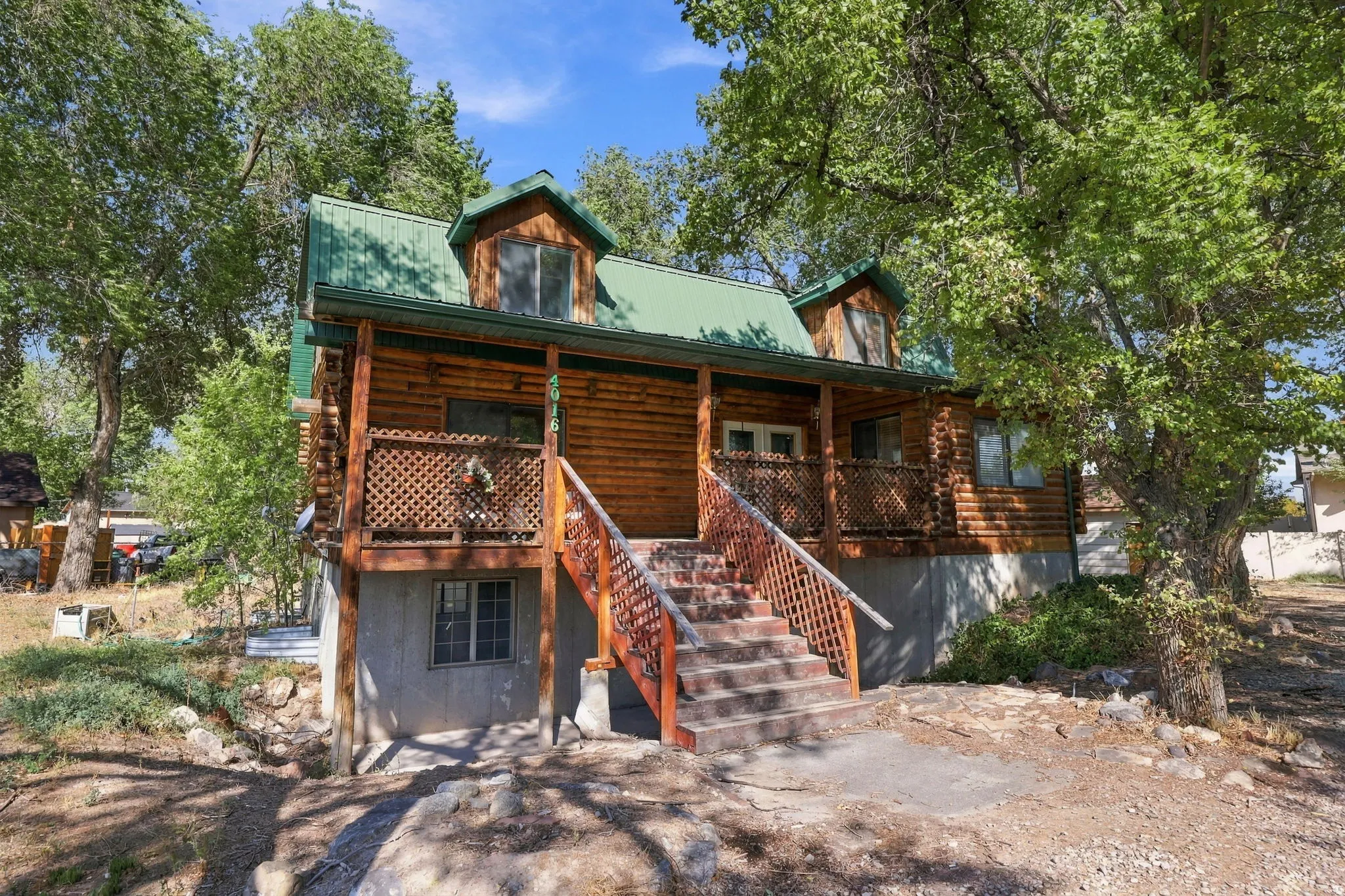 Log cabin exterior featuring a green metal roof, front porch with wood railings, and dormer windows