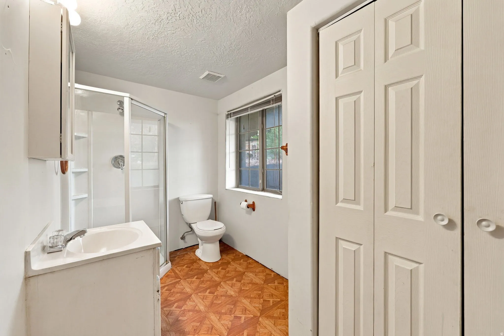 White vanity with an integrated sink, walk-in shower with glass enclosure, toilet, and patterned wood-finish flooring