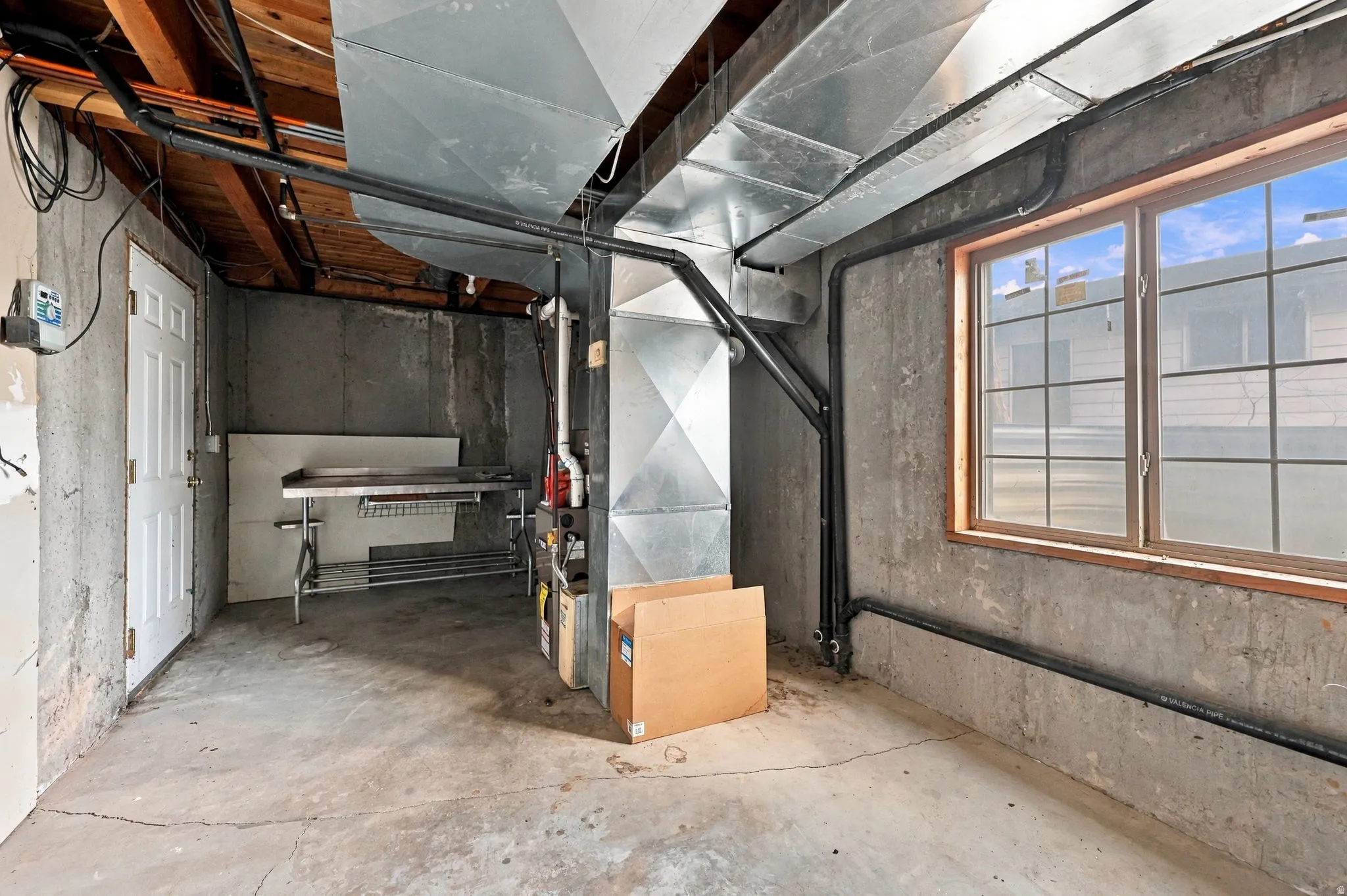 Concrete flooring and walls, exposed ceiling joists, and a window with grid pattern