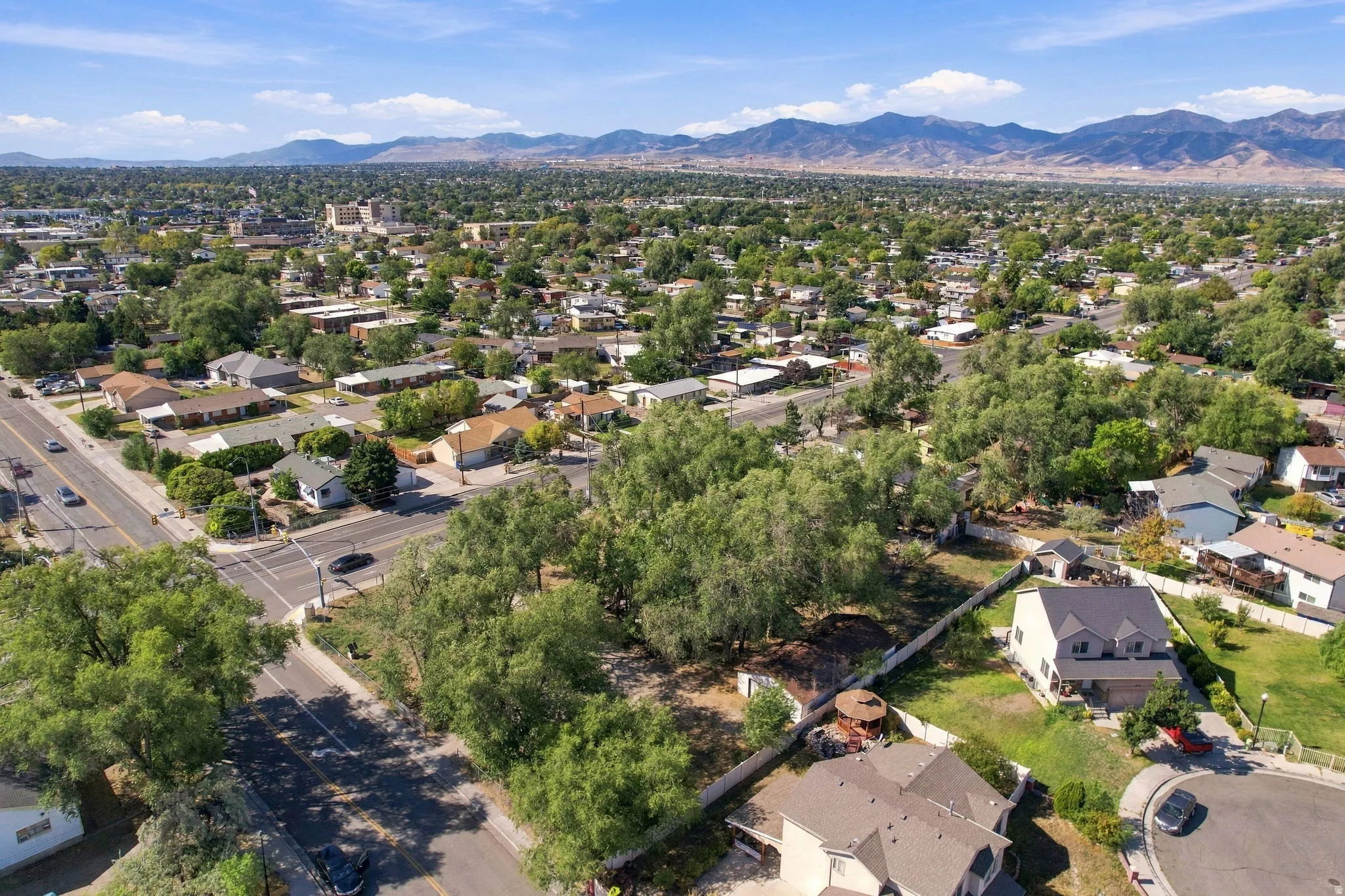 Expansive lot featuring mature trees, a surrounding neighborhood, and distant mountain backdrops