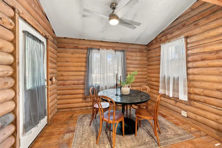 Log wall construction, wood-finish flooring, white ceiling, ceiling fan with integrated lighting, and a white door with glass insert