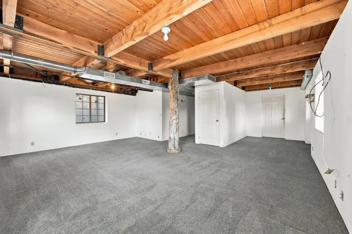Exposed wood beam ceiling, carpet flooring, multiple white doors, exposed ductwork, and a single-pane window