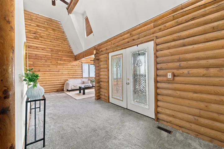 Double entry doors with decorative glass panels, full log wall construction, and a sloped ceiling with exposed wood beams