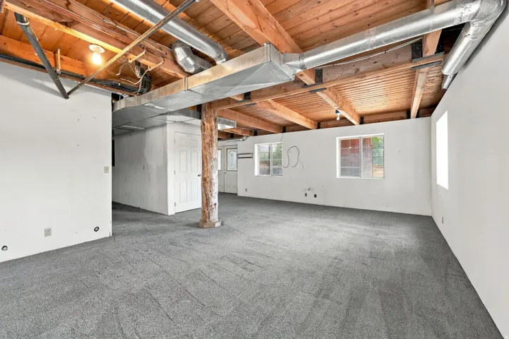 Exposed wood beam ceiling with ductwork and lighting, light gray carpet flooring, white walls, and multiple windows