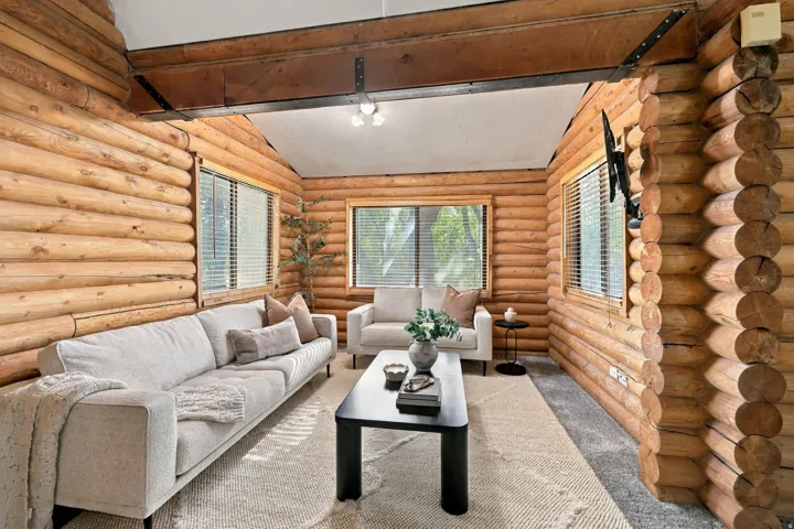 Exposed log walls, vaulted ceiling with exposed beams, wood-framed windows, and track lighting