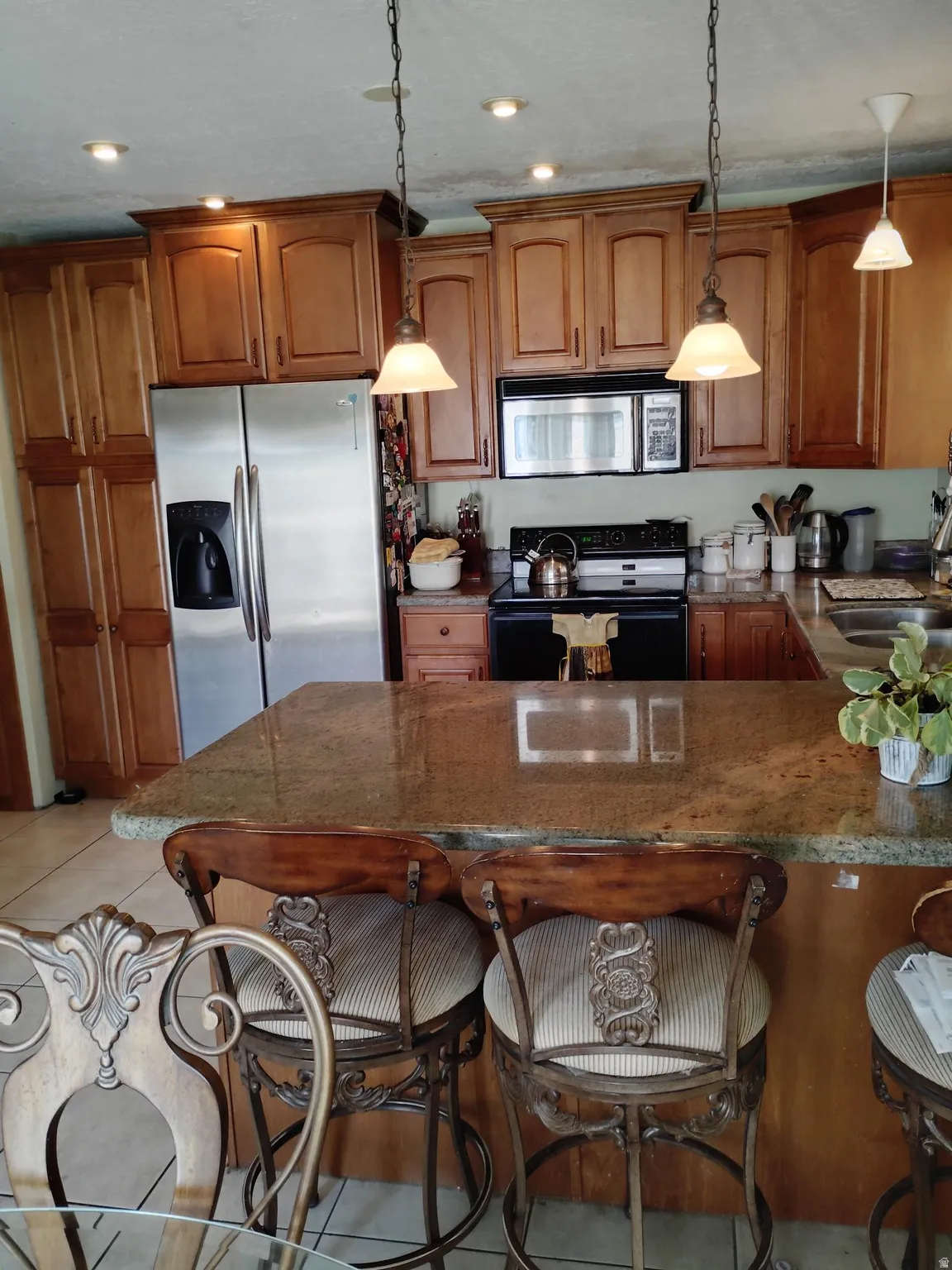 Kitchen featuring wood cabinetry, stainless steel refrigerator, microwave, and a granite-finish island with pendant lighting