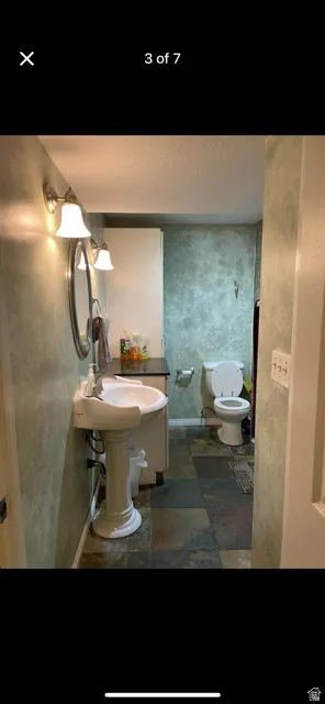 Pedestal sink with an oval mirror, wall-mounted light fixture, and slate tile flooring