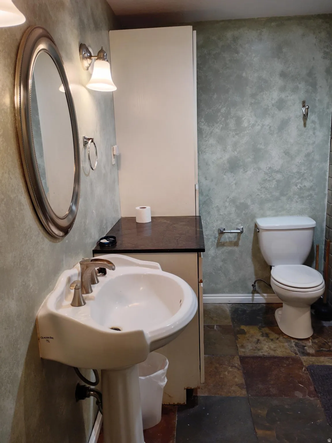 Pedestal sink with brushed nickel faucet, wall-mounted mirror, and vanity lighting