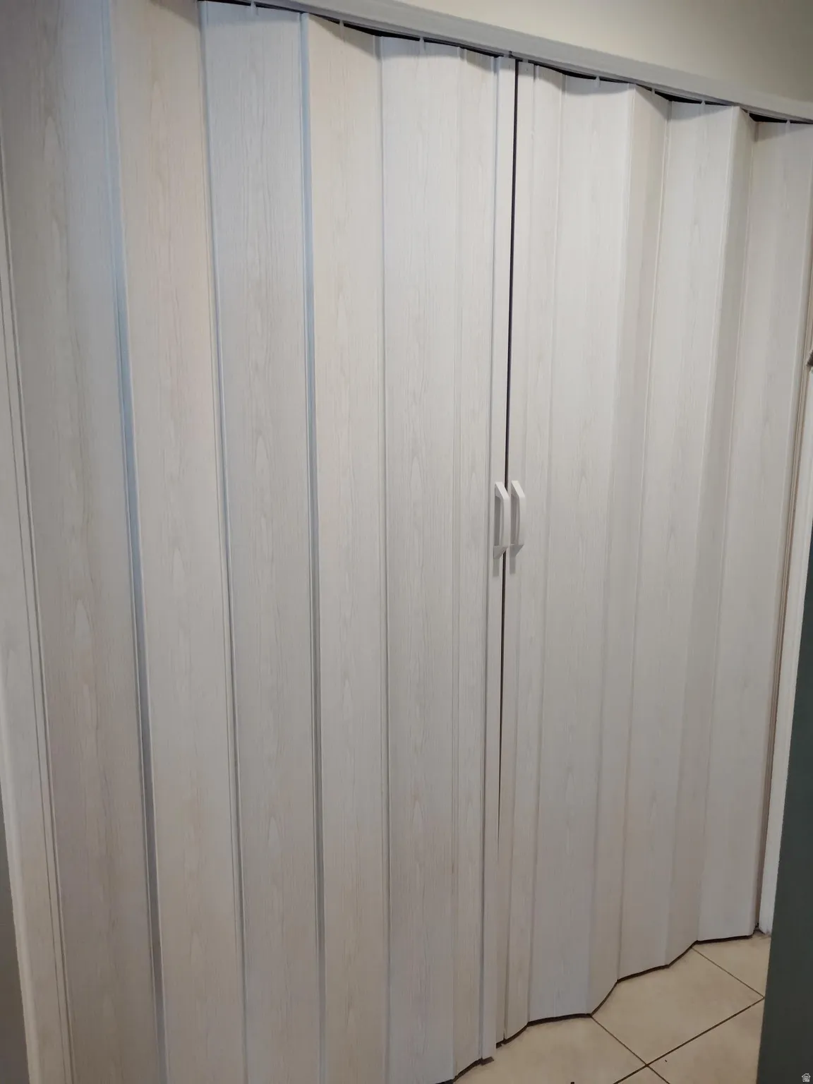 White wood-finish accordion doors with dual handles and a top track system