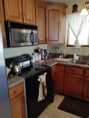 Wood cabinetry, stainless steel over-the-range microwave, built-in electric range, and solid surface countertops