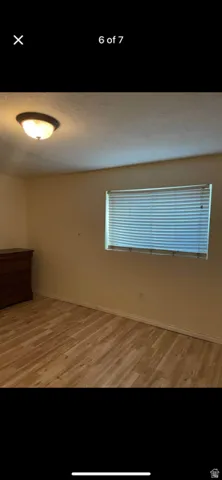 Wood-finish flooring with a window featuring horizontal blinds and a ceiling-mounted light fixture