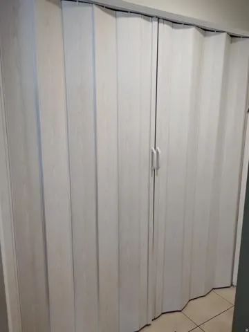 White wood-finish accordion doors with dual handles and a top track system