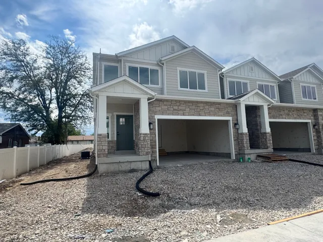 New construction townhome featuring stone and siding exterior finishes, a covered entryway with columns, a dark-paneled front door, and an attached two-car garage
