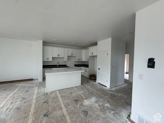 Kitchen featuring white cabinetry with dark hardware, dark countertops, a center island with a light-colored countertop, and recessed lighting