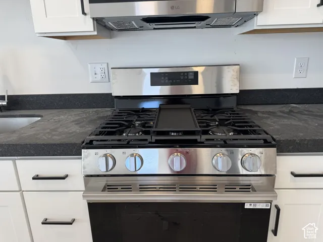 Stainless steel range with a griddle, dark countertops, white cabinetry, and a stainless steel microwave