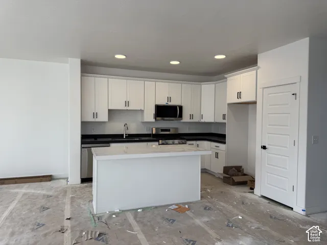 White shaker cabinetry, recessed lighting, black countertops, stainless steel appliances, and a central island