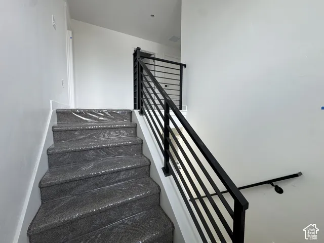 Staircase featuring dark carpeted steps and a contemporary black metal horizontal railing