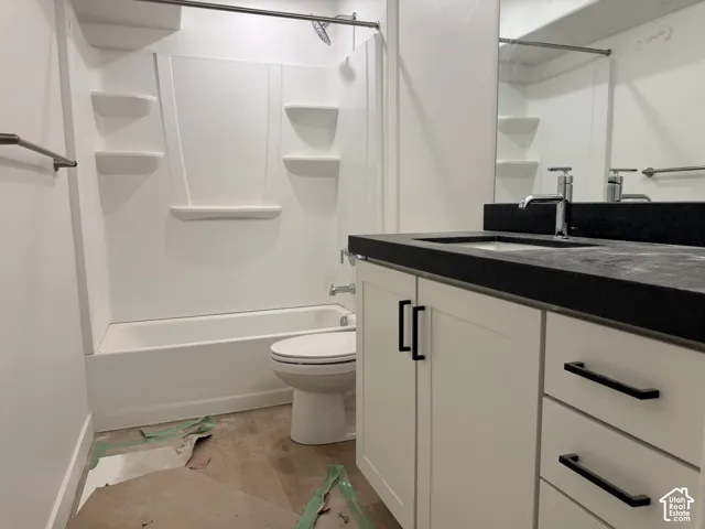 White bathtub with integrated shelving, chrome showerhead, white vanity with black countertop, integrated sink, and black hardware