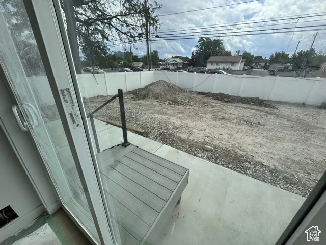 Sliding glass door leading to a concrete patio with composite decking and a black metal handrail, enclosed by a white vinyl fence