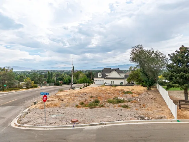 Corner lot featuring a white picket fence, adjacent road frontage, and a distant mountain range