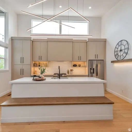 Vaulted ceiling with linear lighting, contemporary kitchen cabinetry, stainless steel appliances, central island with integrated seating, and light wood-finish flooring