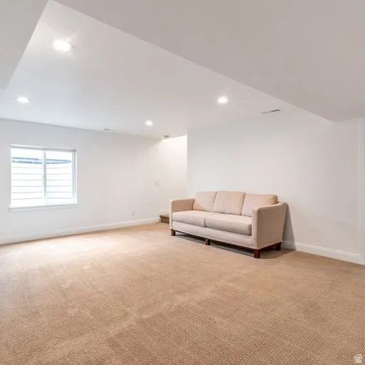 Recessed lighting, white walls, and a window with horizontal blinds complement the neutral carpeting