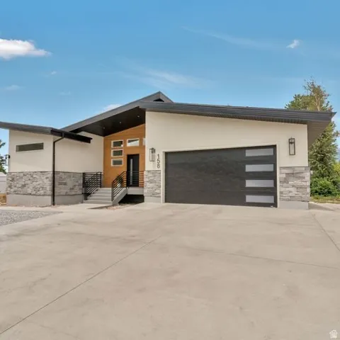 Contemporary exterior featuring a black garage door with frosted panels, a stone veneer facade, and a concrete driveway