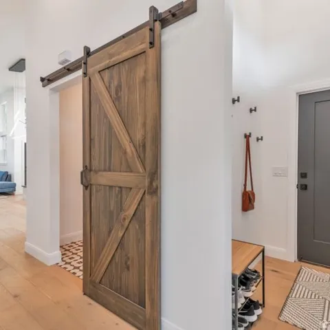 Wood-finish barn door with dark hardware, light wood-finish flooring, and a dark entry door