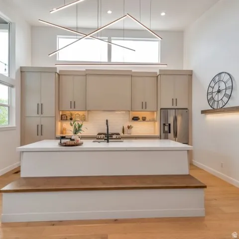 Vaulted ceiling with linear lighting, contemporary kitchen cabinetry, stainless steel appliances, central island with integrated seating, and light wood-finish flooring