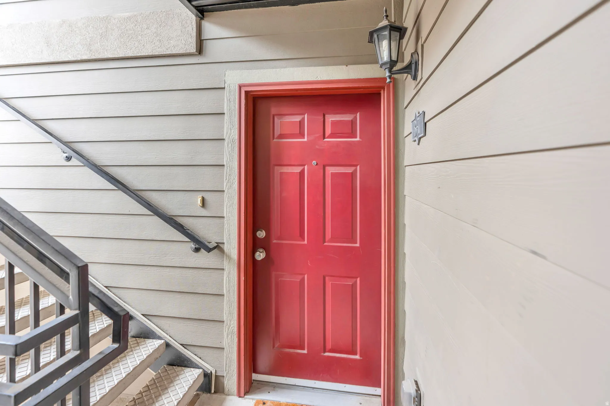 Welcoming entry featuring a bold red six-panel door with polished hardware, white trim frame, and a wall-mounted light fixture