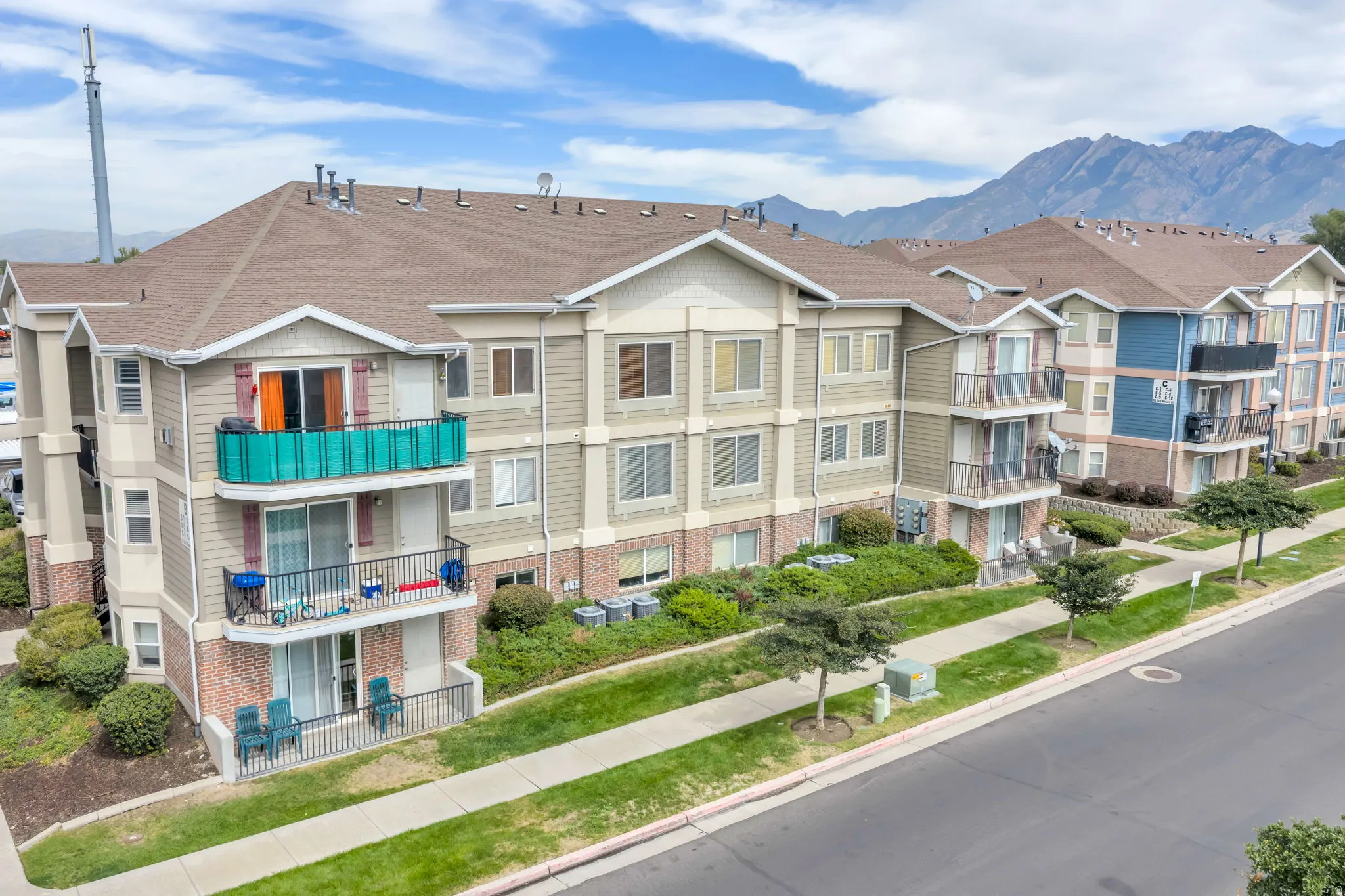 Multi-story residential building featuring balconies, brick and siding exterior, and a paved walkway