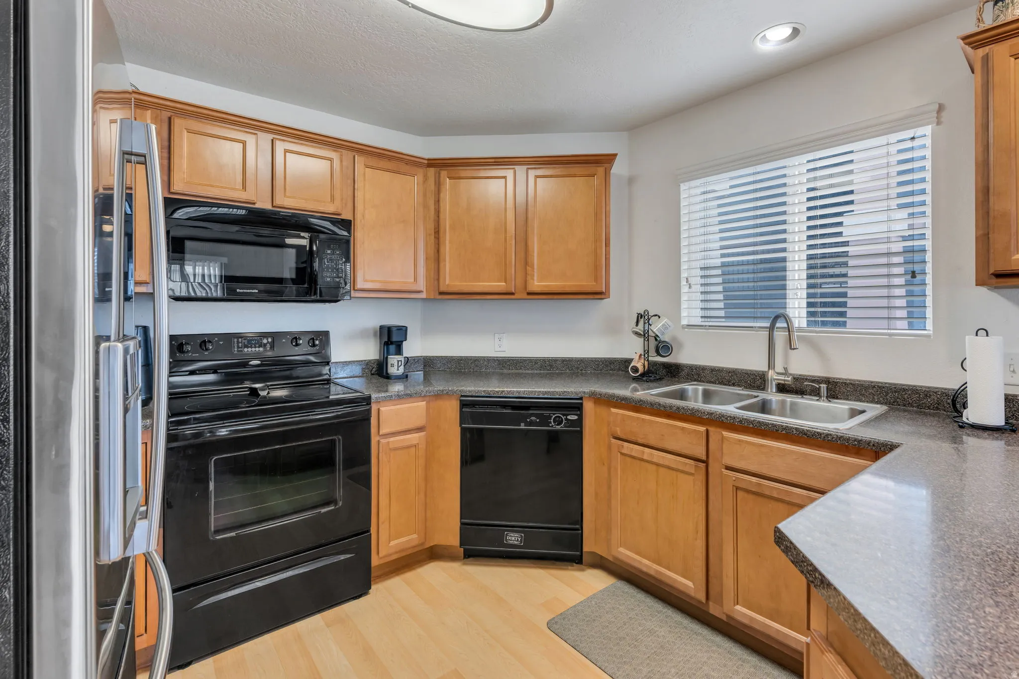 Kitchen featuring wood-finish cabinetry, black appliances, a double basin sink, and a counter with a textured surface