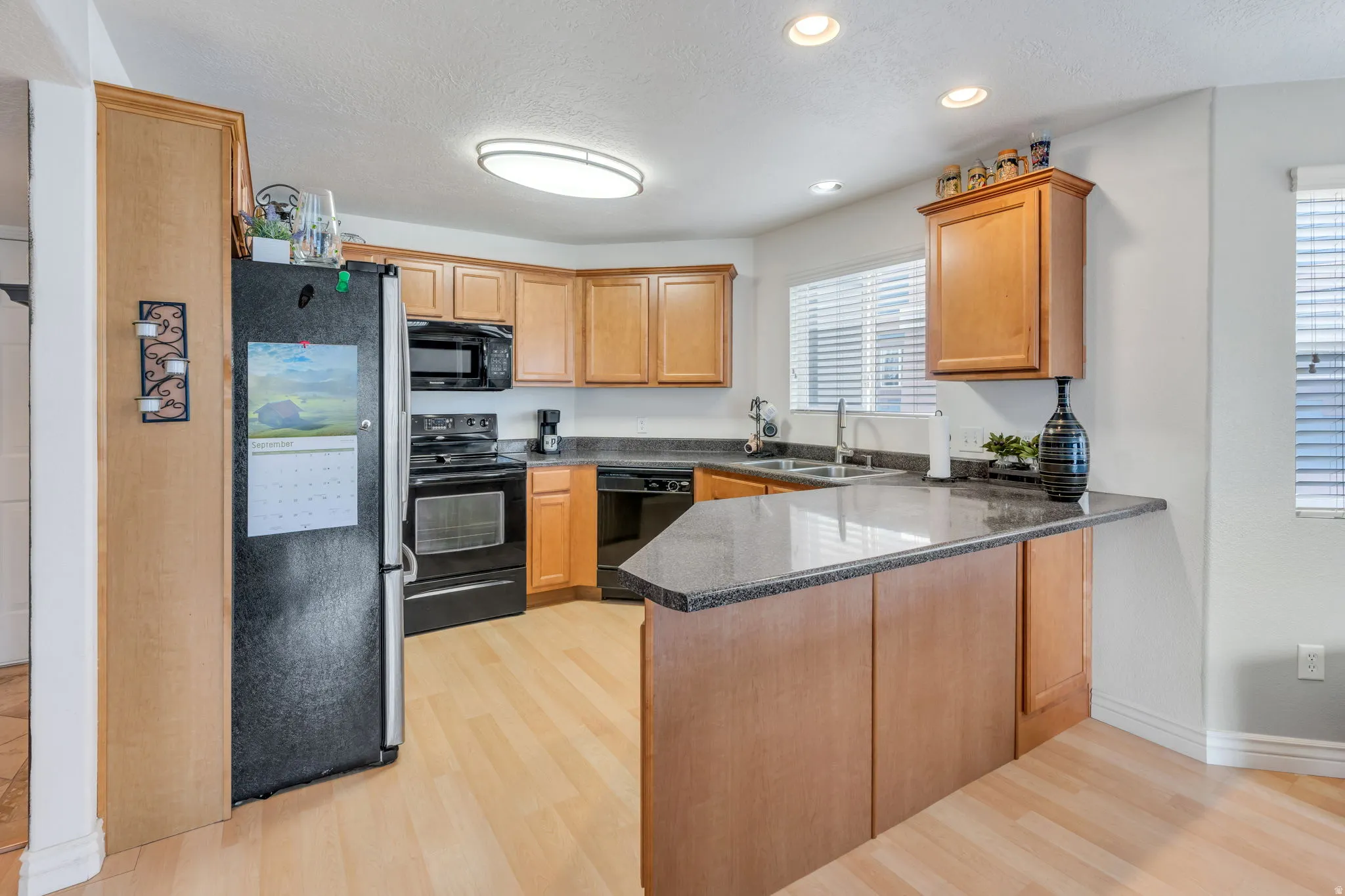 Kitchen featuring wood-finish cabinetry, dark countertops, black appliances, and a breakfast bar