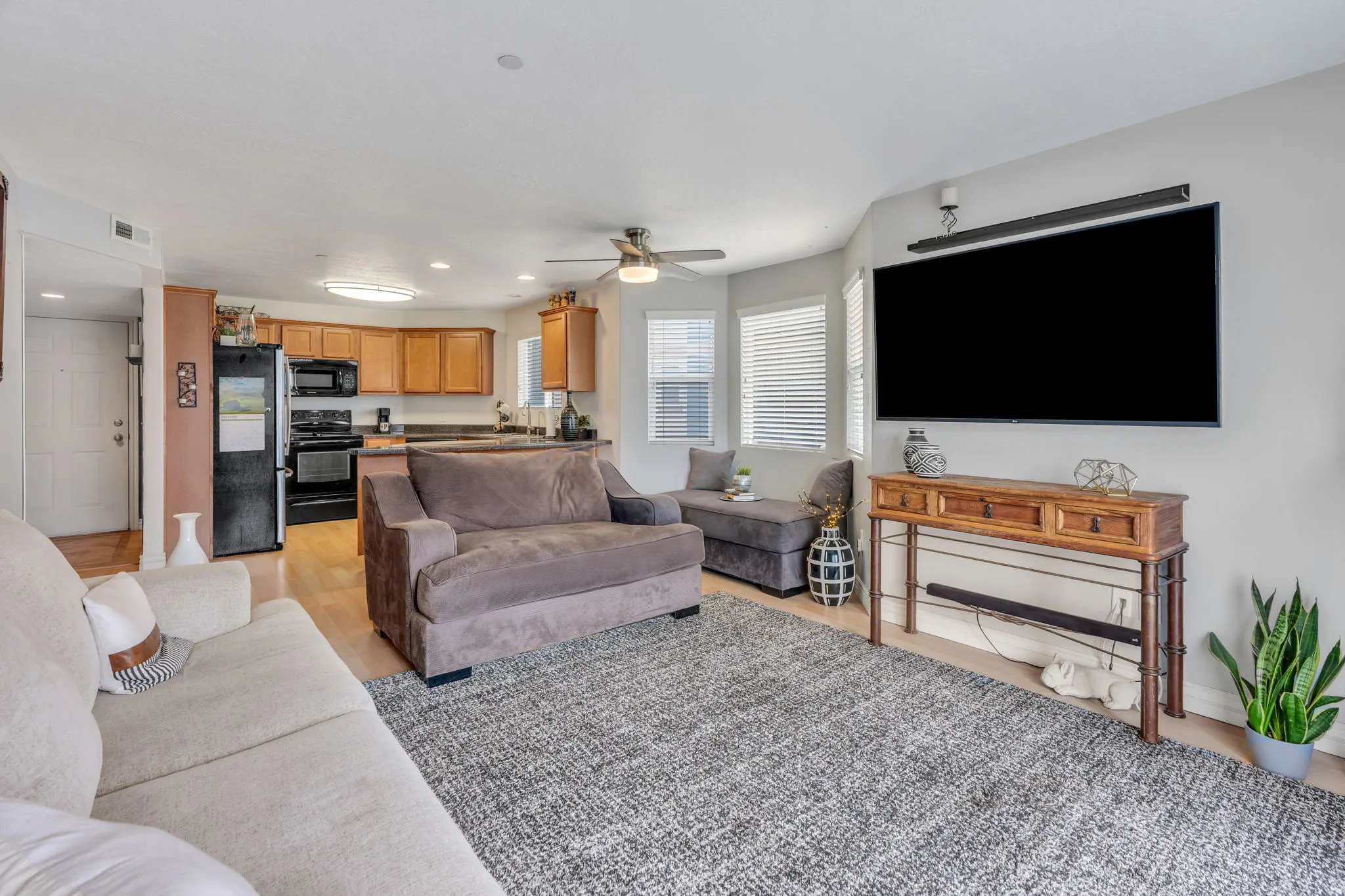 Open-concept living area with wood-finish flooring, a ceiling fan, and multiple windows with blinds
