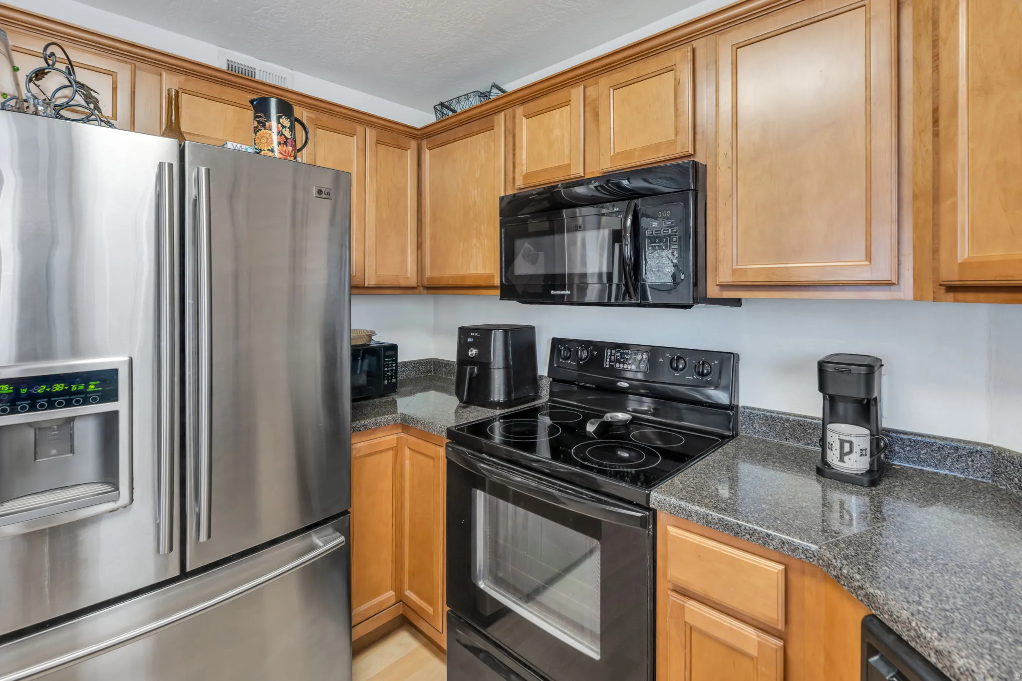 Stainless steel refrigerator with a water/ice dispenser, black range, black built-in microwave, wood-finish cabinetry, and speckled countertops