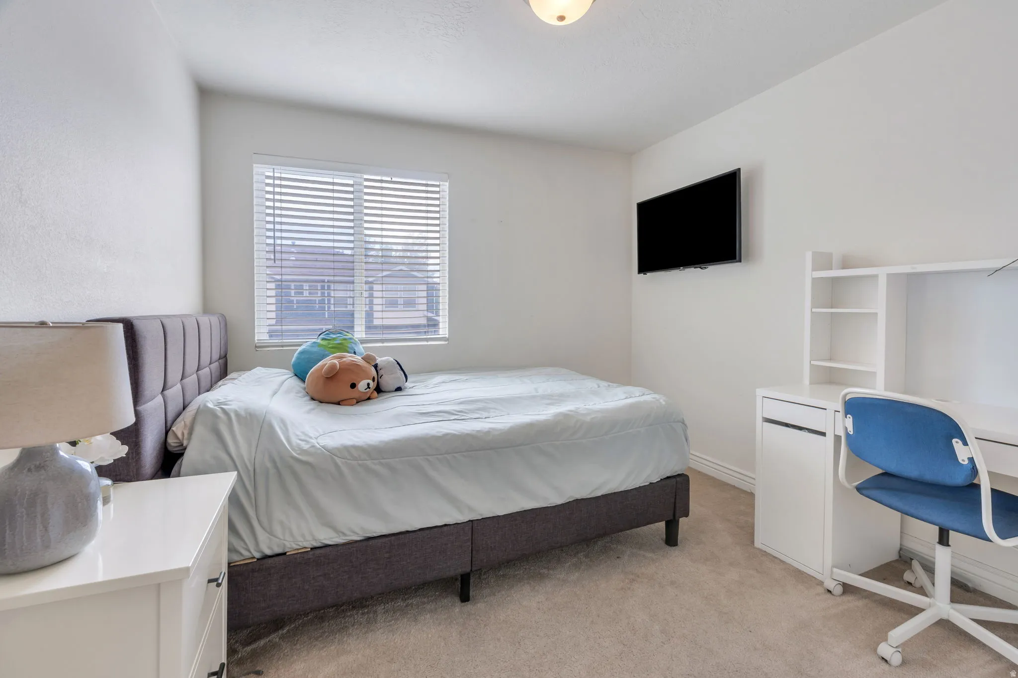 Carpeted room with a ceiling-mounted light fixture, a window featuring blinds, and a built-in white desk with shelving