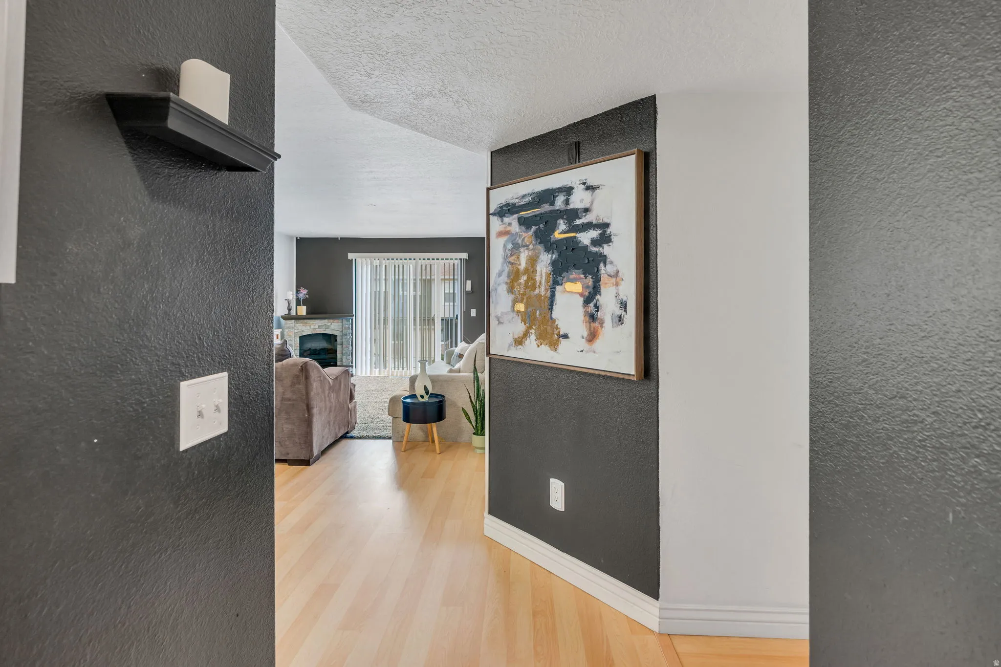 Bright interior with light wood-finish flooring, dark accent walls, and a fireplace with a stone surround