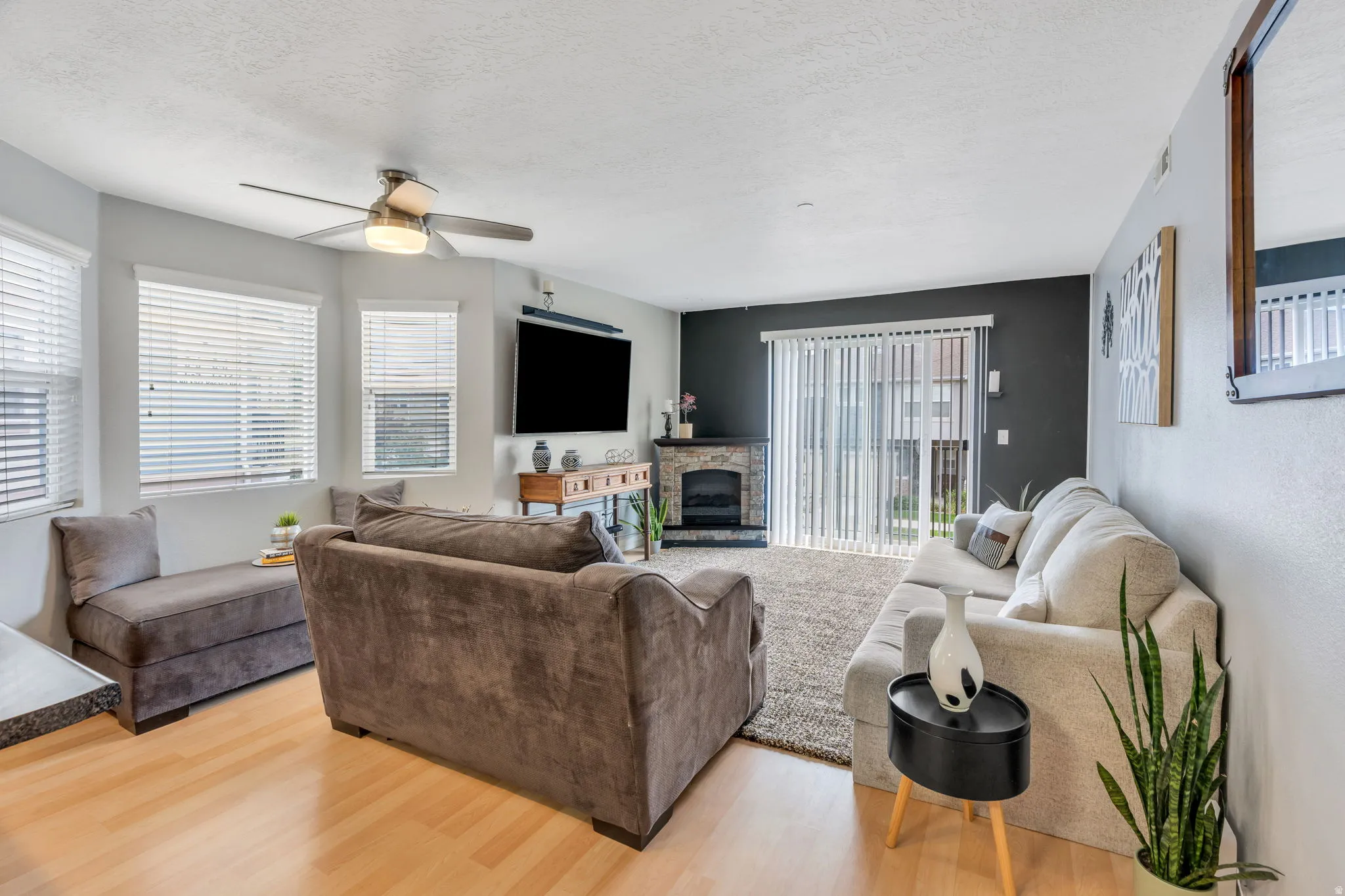 Hardwood-style flooring throughout, bay windows with blinds, a built-in fireplace, a ceiling fan with integrated lighting, and a sliding glass door