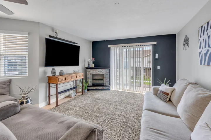 Living area with wood-finish flooring, a stone-clad corner fireplace, and vertical blinds on the sliding glass door
