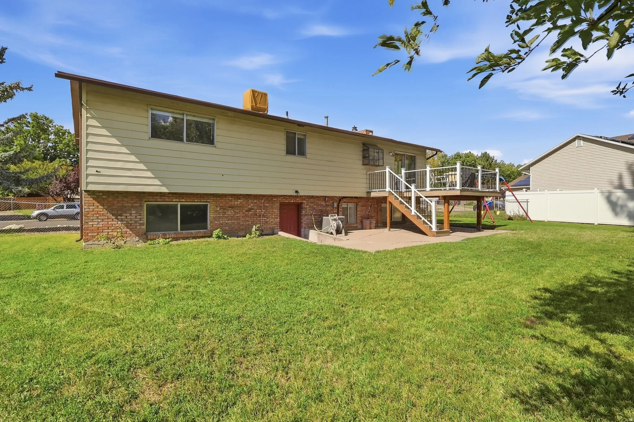Expansive green lawn, multi-level wood deck, white railing, brick lower exterior, horizontal siding upper exterior