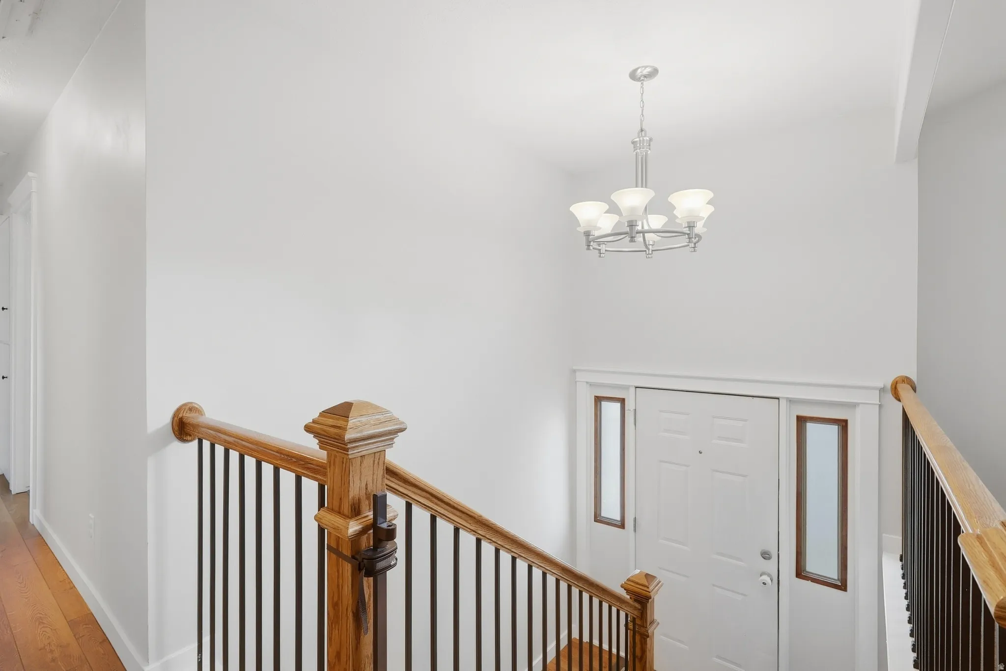 Wood-finish flooring, staircase with wood newel post and metal balusters, entry door with sidelights, and a chandelier with frosted glass shades