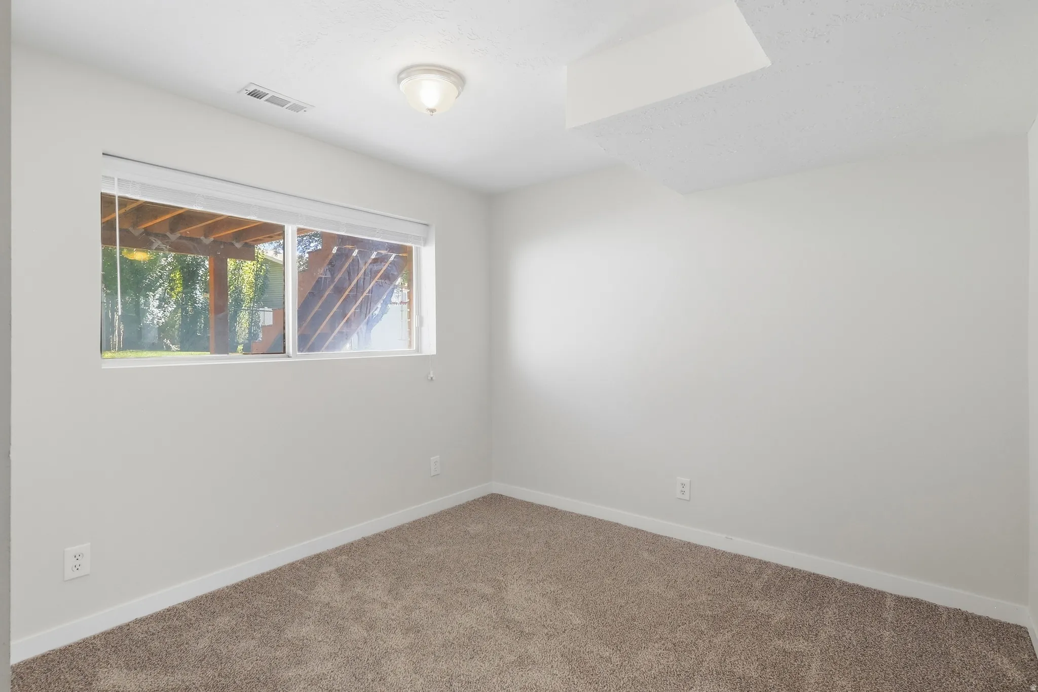 Wall-to-wall carpeting with light-toned walls, featuring a window with integrated blinds