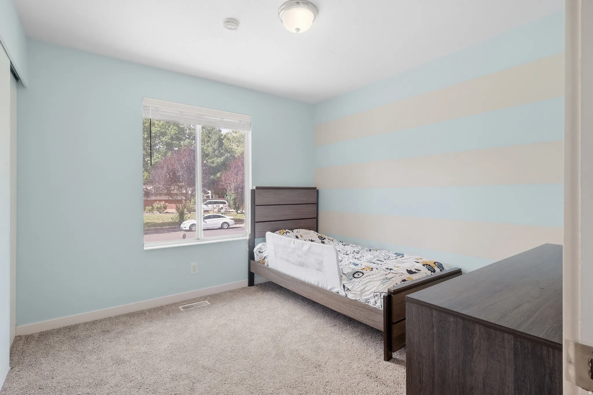 Carpeted flooring, light blue and striped accent walls, ceiling-mounted lighting fixture, and a window with blinds