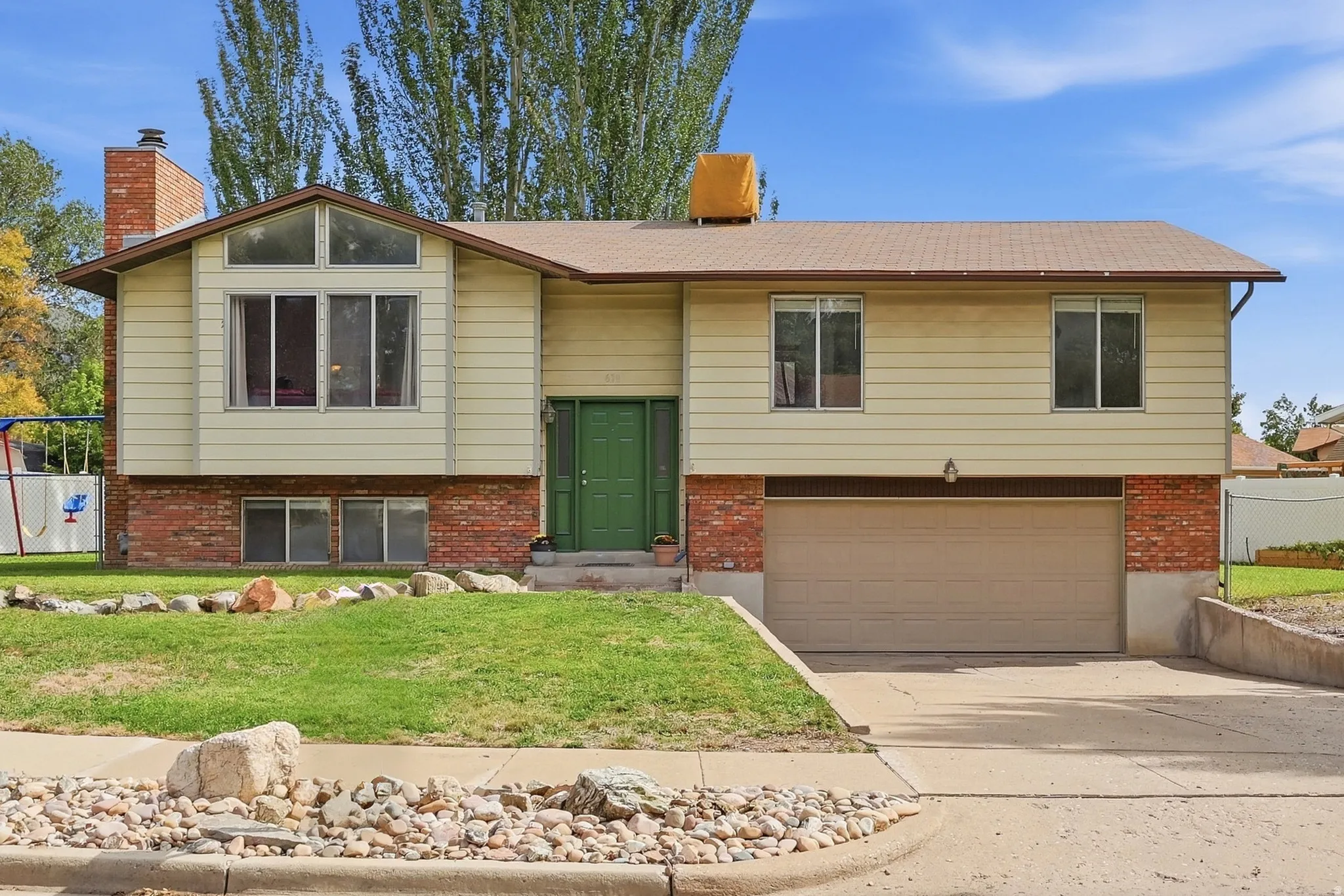 Split-level residence featuring a brick and siding exterior, an attached garage, a driveway, and a front lawn with a rock border