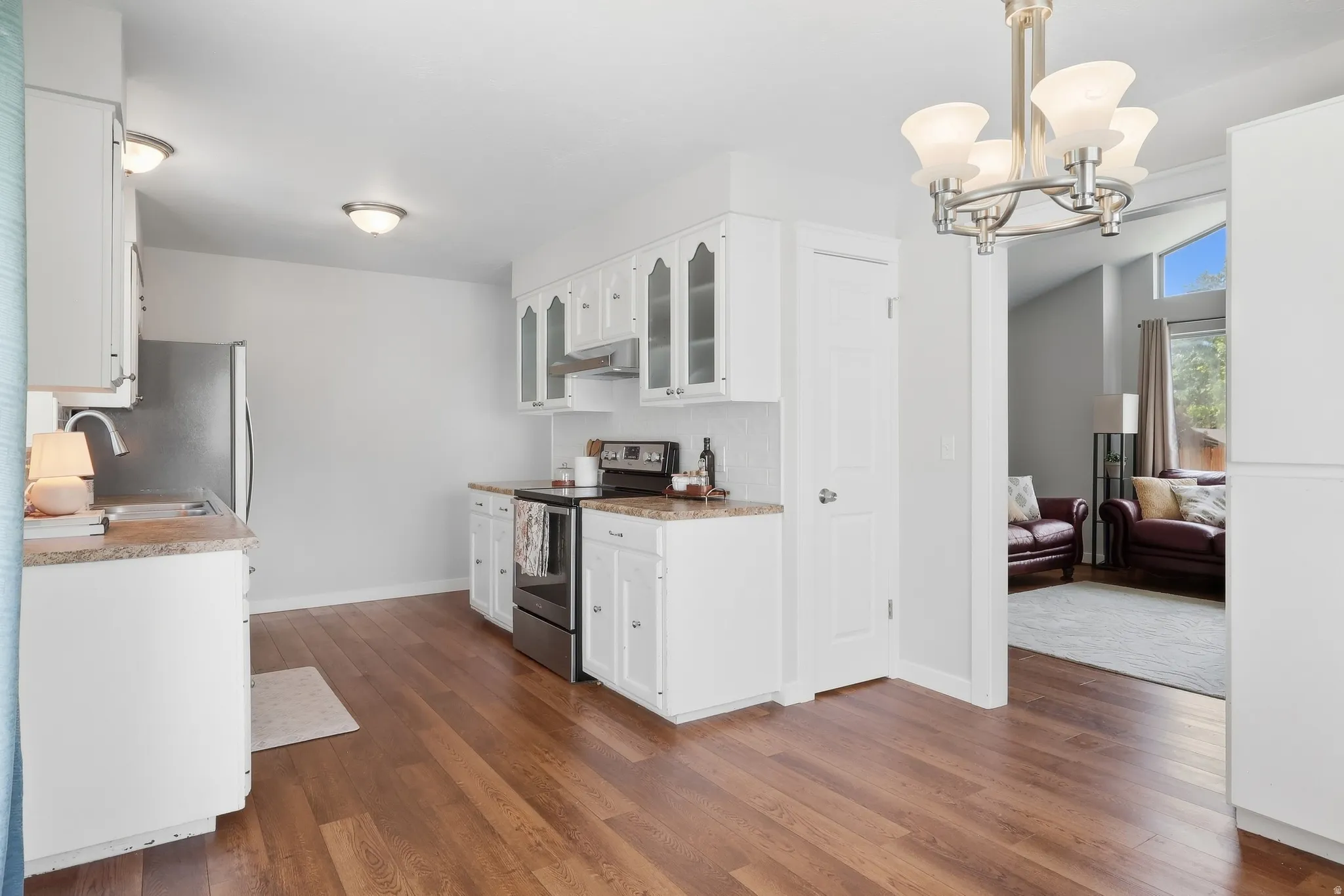 Open kitchen featuring white cabinetry with glass-front upper cabinets, stainless steel appliances, wood-finish flooring throughout, and a central island layout