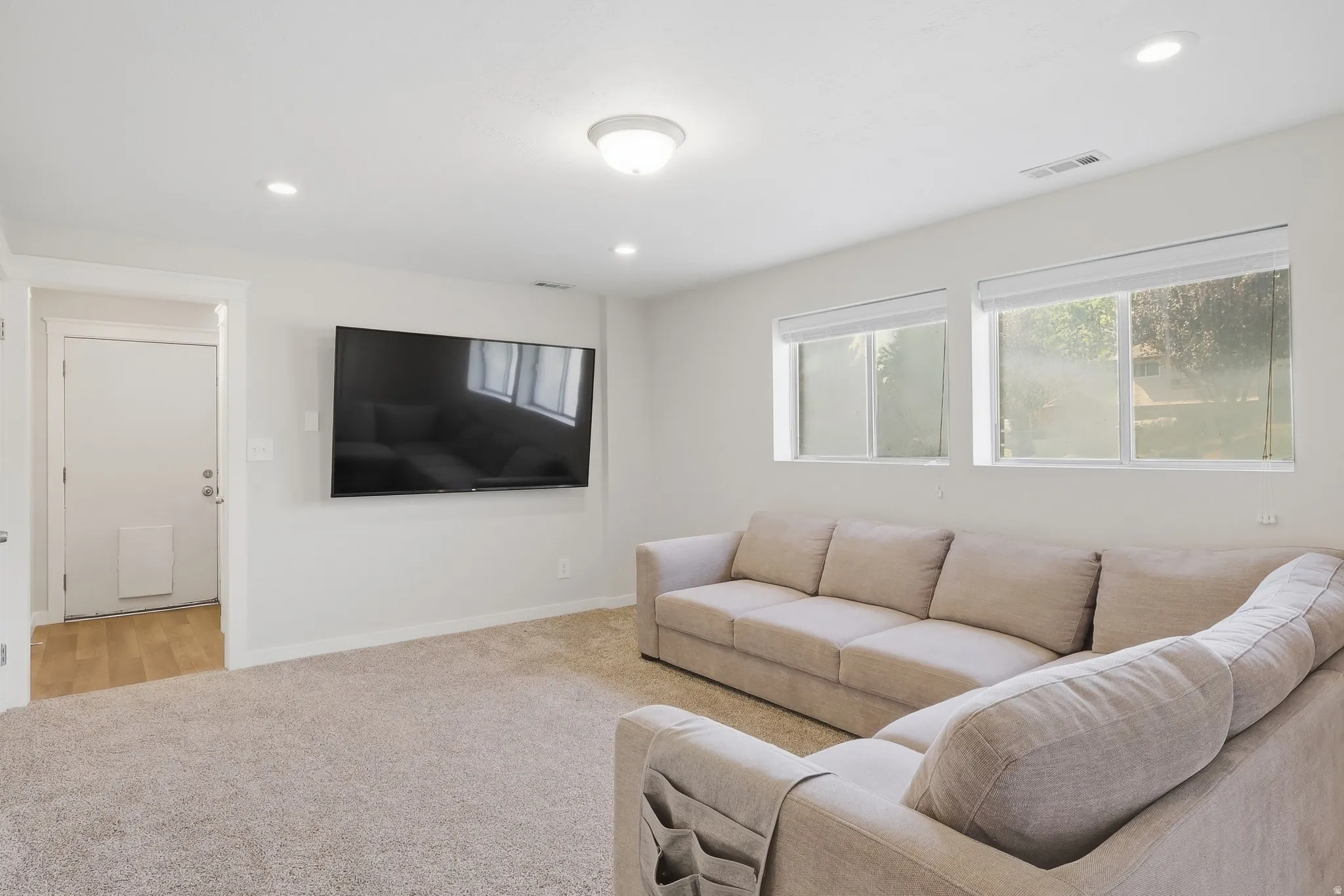 Neutral tone carpeting, dual flush-mounted ceiling lights, recessed lighting, and multiple windows with roller shades
