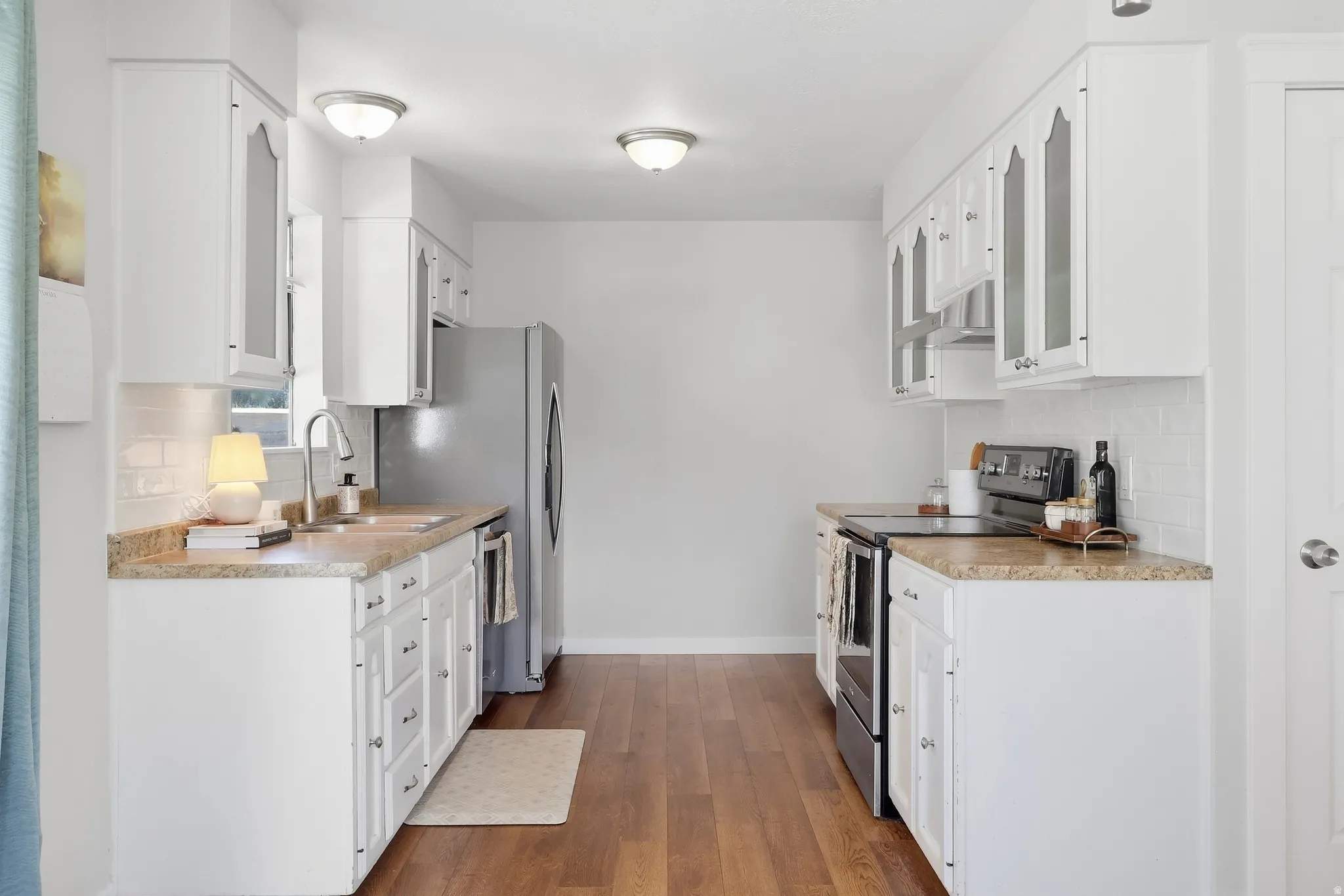 Bright kitchen featuring white cabinetry, wood-finish flooring, a stainless steel refrigerator, stone-look countertops, and a subway tile backsplash