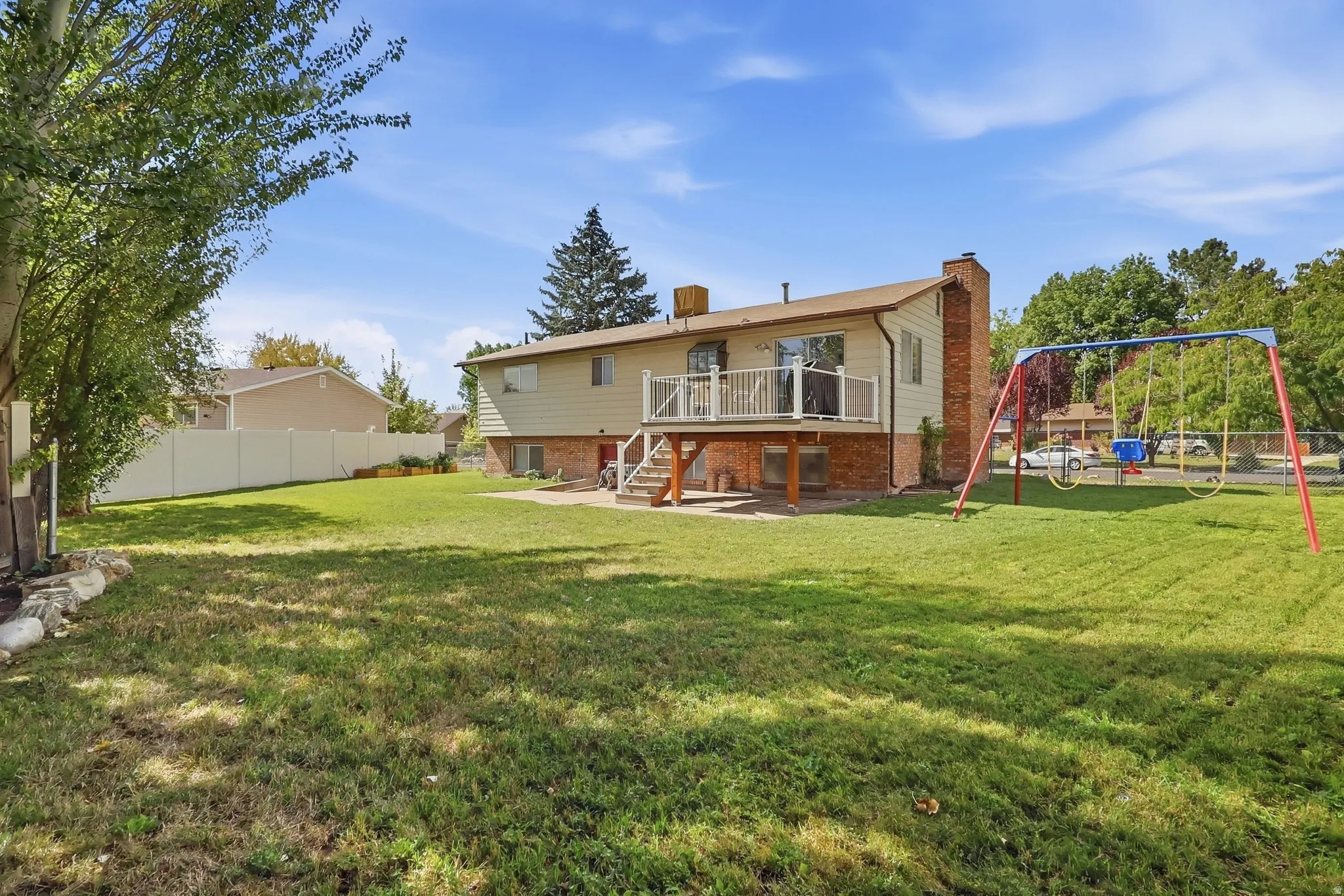 Expansive backyard featuring a large elevated deck, ground-level patio, and a brick chimney exterior